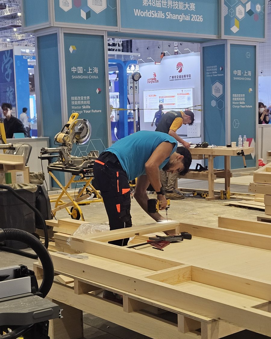 Ein Teilnehmer verschraubt eine Holzkonstruktion unter dem WorldSkills-Bogen in Shanghai 2026